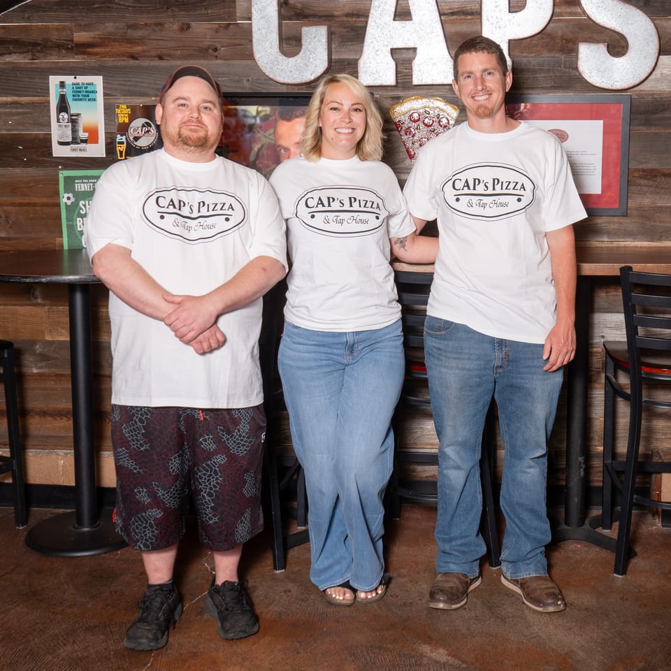 Three Cap's Pizza & Tap House employees smile in their restaurant.
